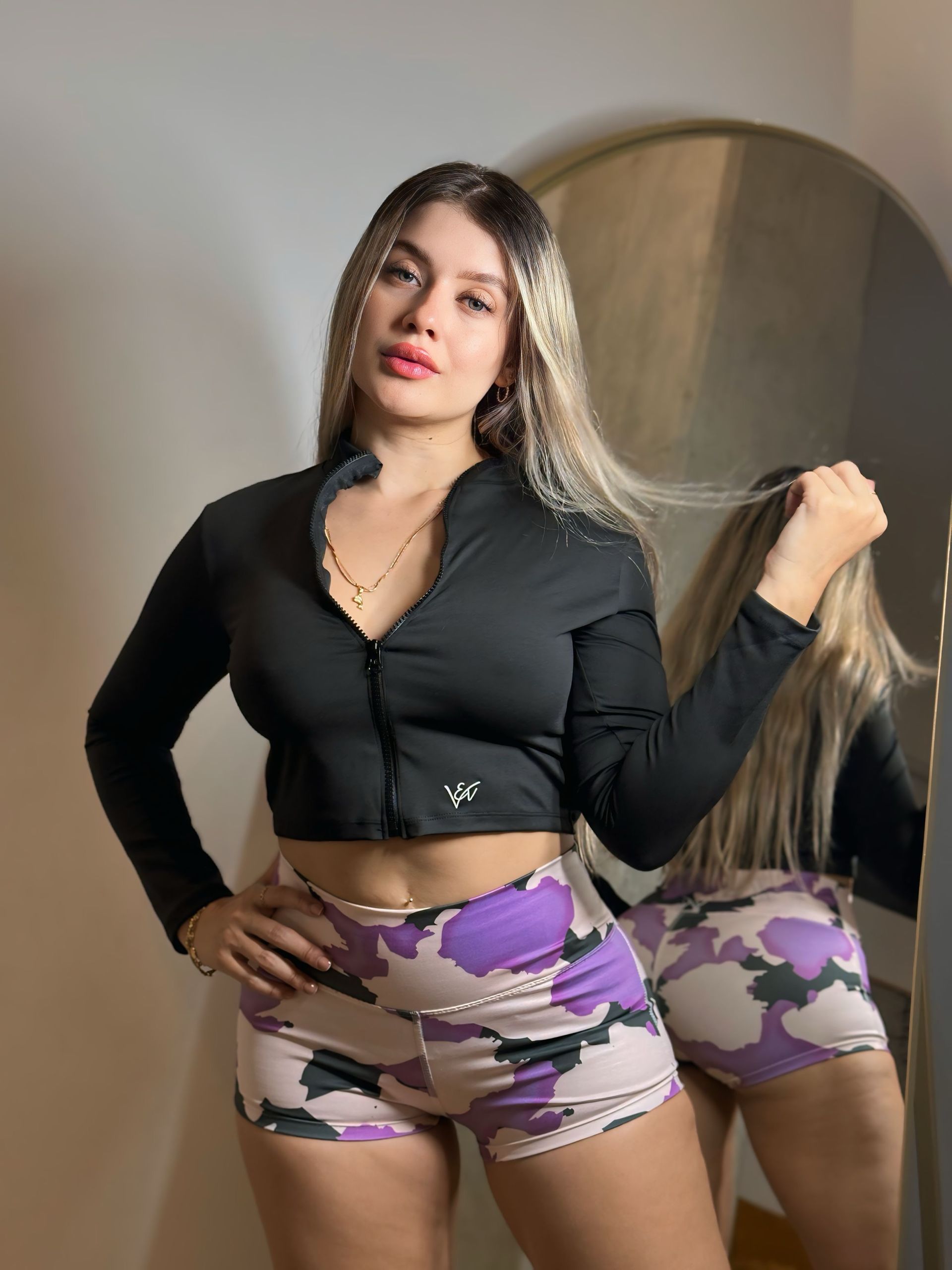 A woman in a black crop top and purple shorts is standing in front of a mirror.
