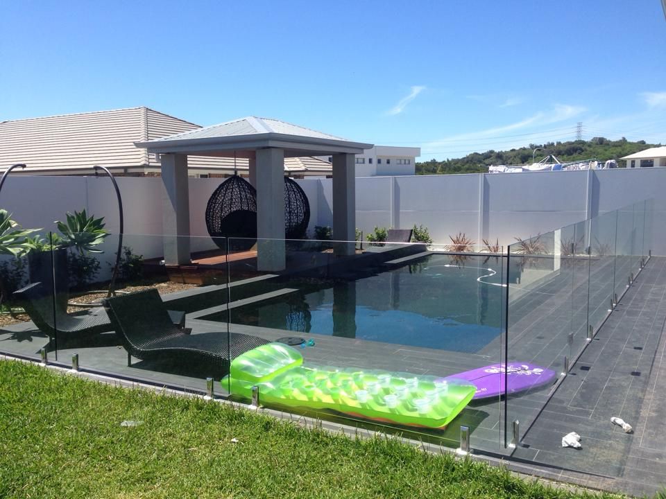 Backyard pool with glass fence, lounge chair, and colorful float under a sunny blue sky — ClearView Glass Pool Fencing In Roselands, NSW