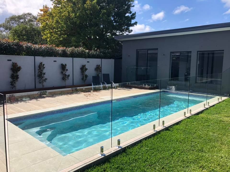 Modern backyard pool with glass safety fence beside a house and green lawn — ClearView Glass Pool Fencing In Roselands, NSW