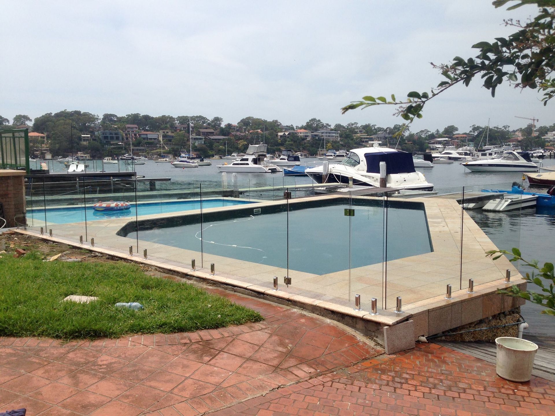 Harbor marina with boats, a dock, and a small pool beside a grassy waterfront walkway — ClearView Glass Pool Fencing In Roselands, NSW