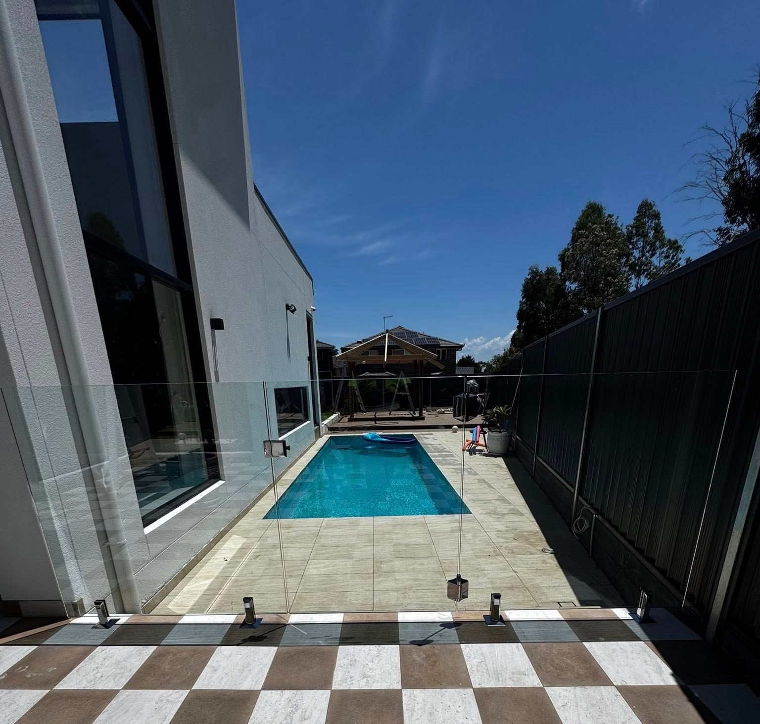 A Backyard Swimming Pool With Blue Tiles and Clear Glass Fencing — ClearView Glass Pool Fencing In Roselands, NSW