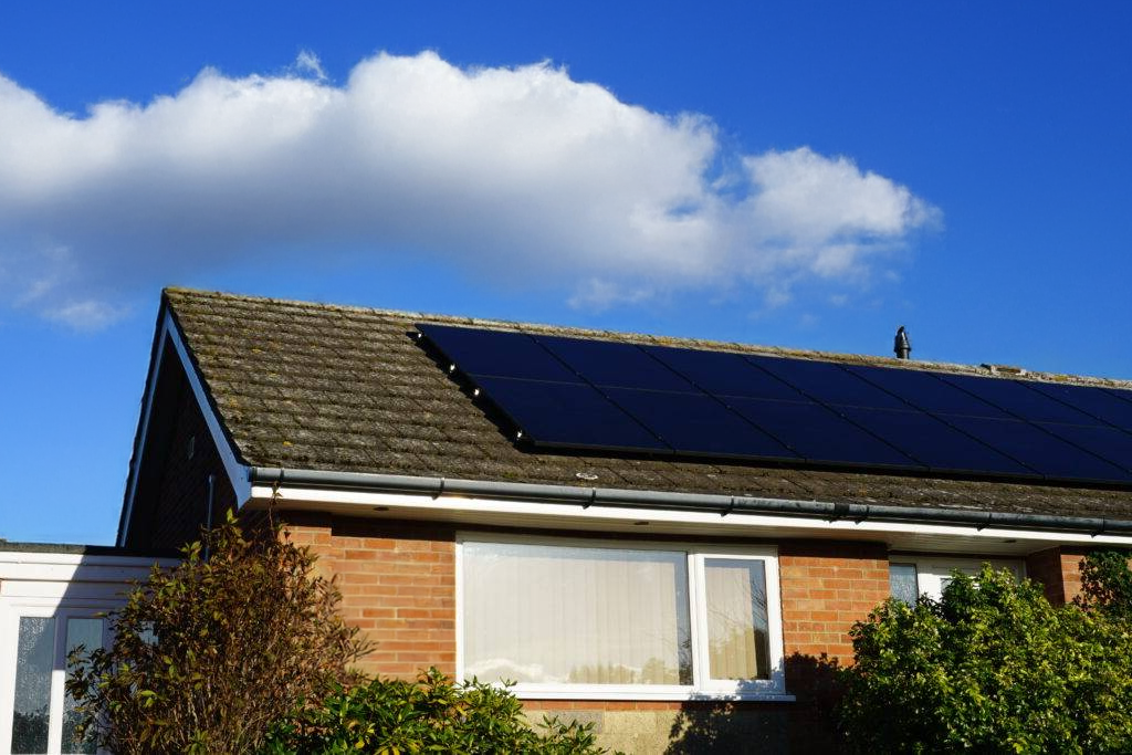 Solar panels on a residential roof against a blue sky with a large cloud.