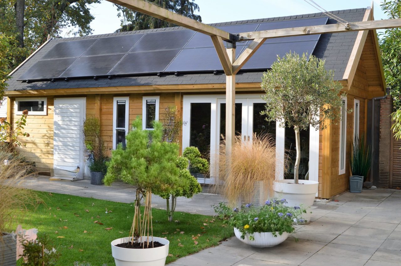 Wooden building with solar panels, glass doors, and potted plants on a patio.