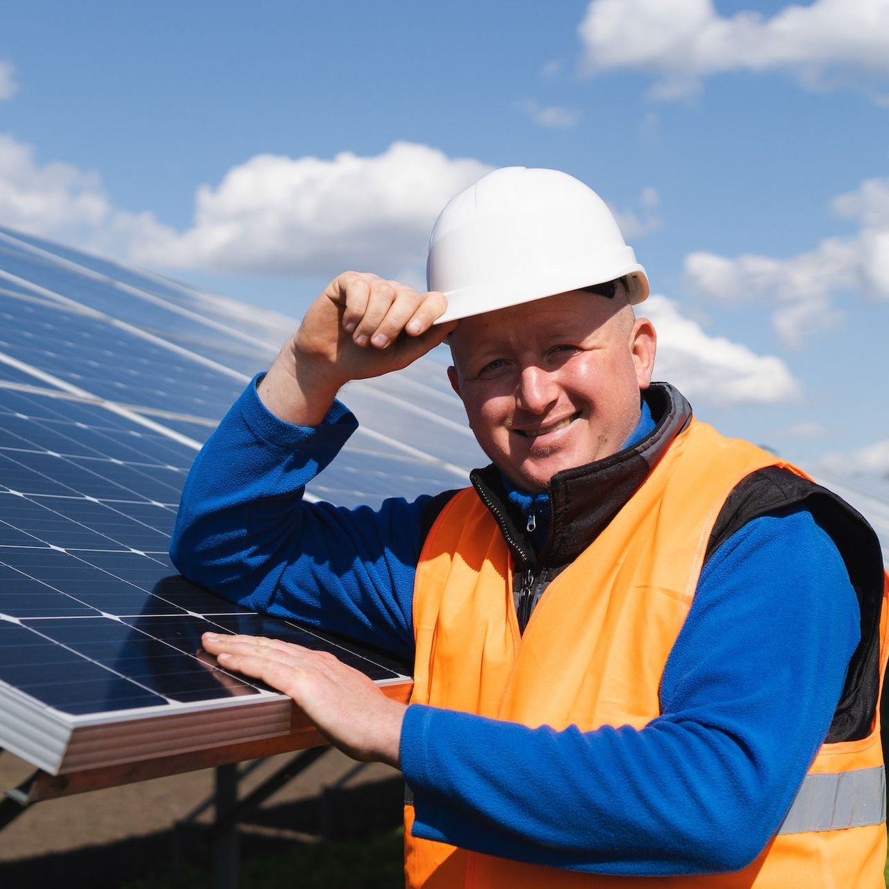 A man wearing a hard hat is standing in front of solar panels