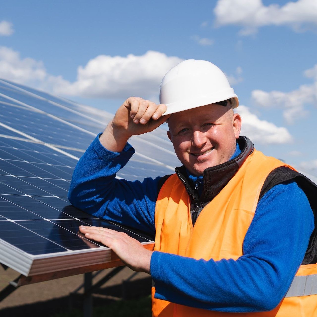 A man wearing a hard hat and an orange vest stands in front of solar panels