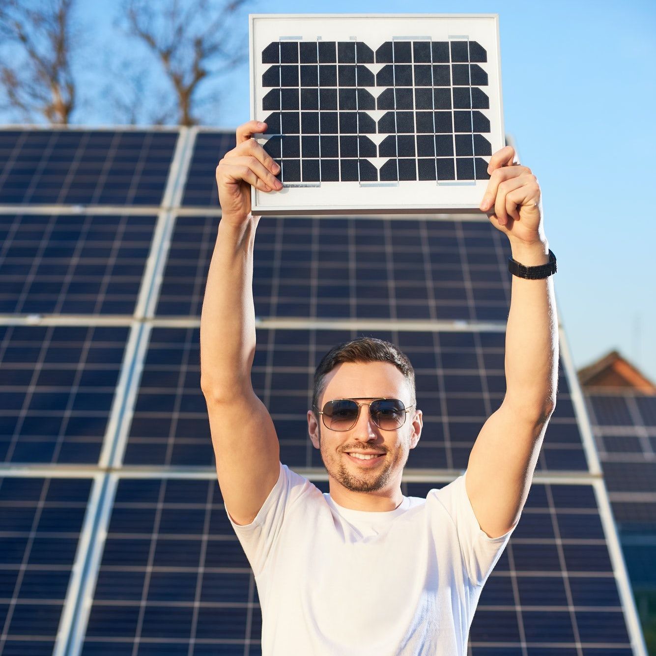 A man is holding a solar panel over his head in front of a solar panel.