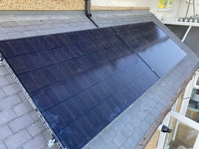 A large solar panel is sitting on top of a slate roof.