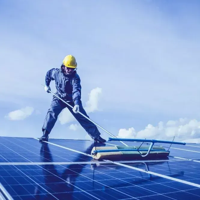 A man is cleaning a solar panel with a broom.