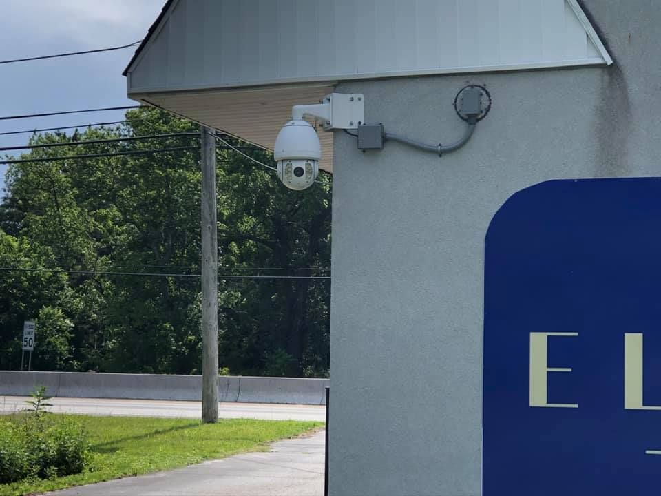 Security camera mounted on a building corner; a street and trees are in the background.
