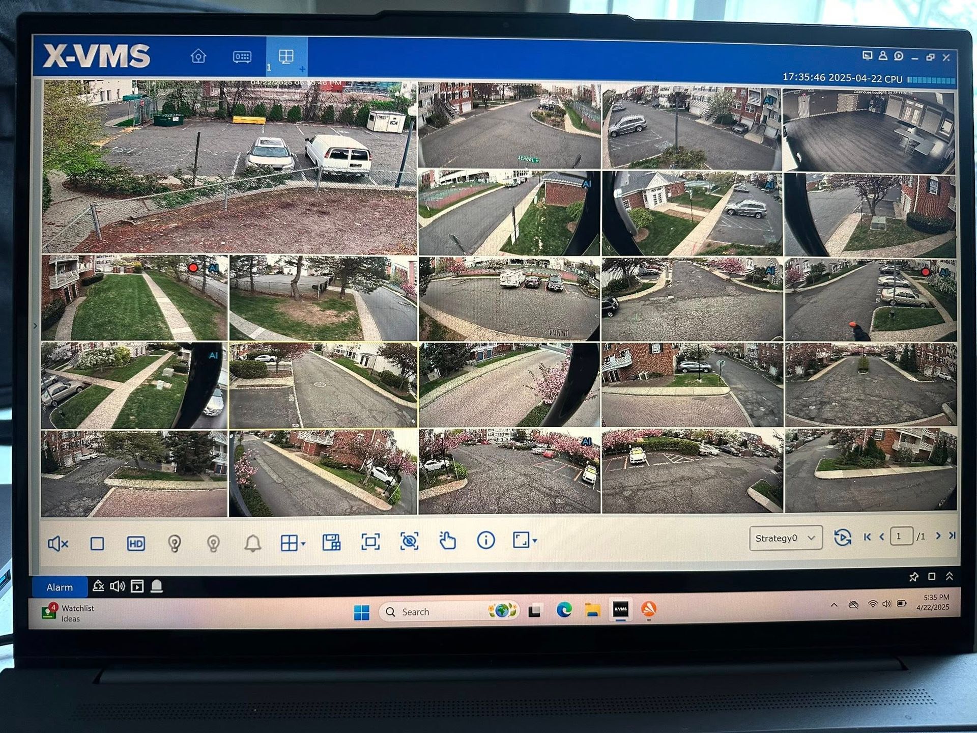 Laptop screen showing a surveillance system, displaying multiple live camera feeds of parking lots and streets.