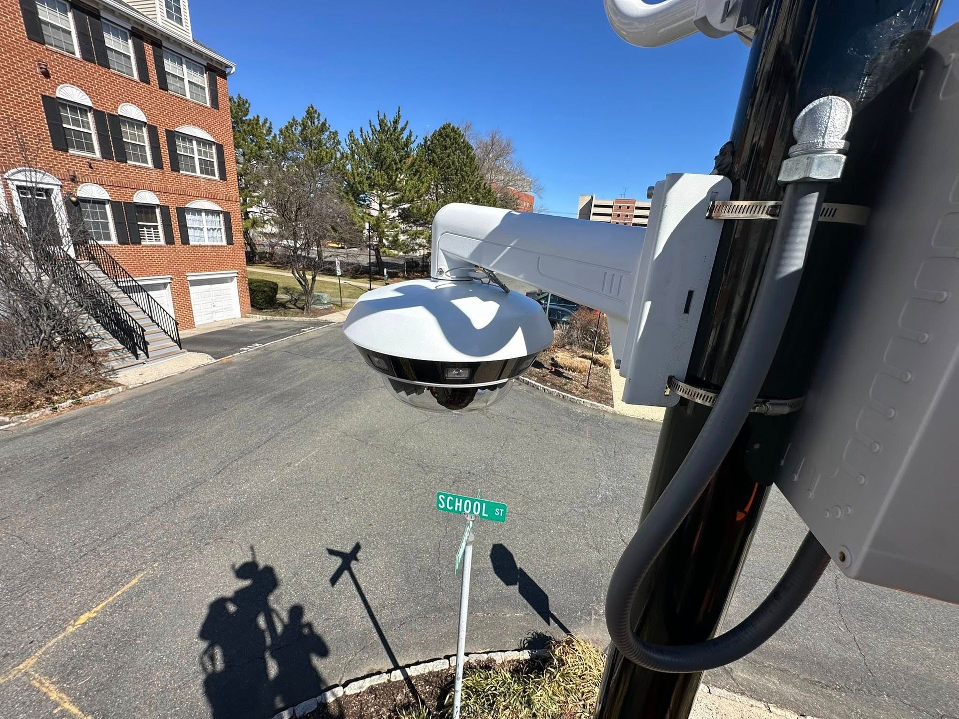 Surveillance camera on a pole overlooking a street and buildings on a sunny day.