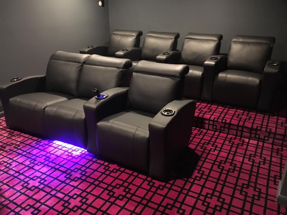 A home theater with black leather recliners and a pink patterned carpet.