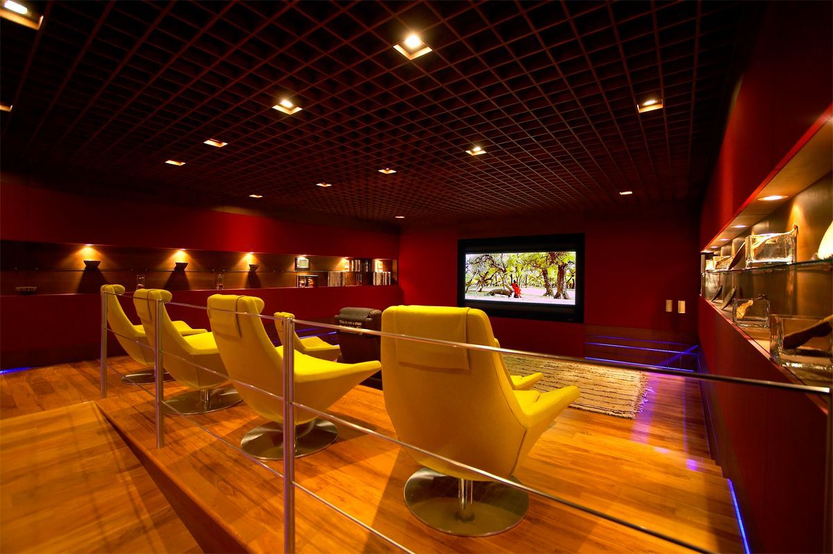 Modern home theater with yellow chairs, red walls, wooden floor, and a screen playing a movie.