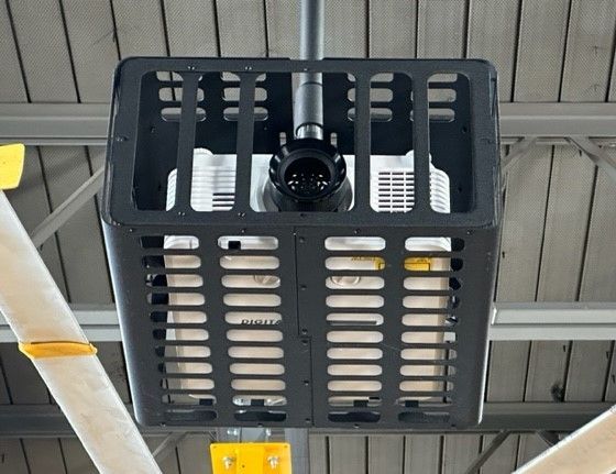 Overhead projector encased in black protective cage, mounted to ceiling in building.