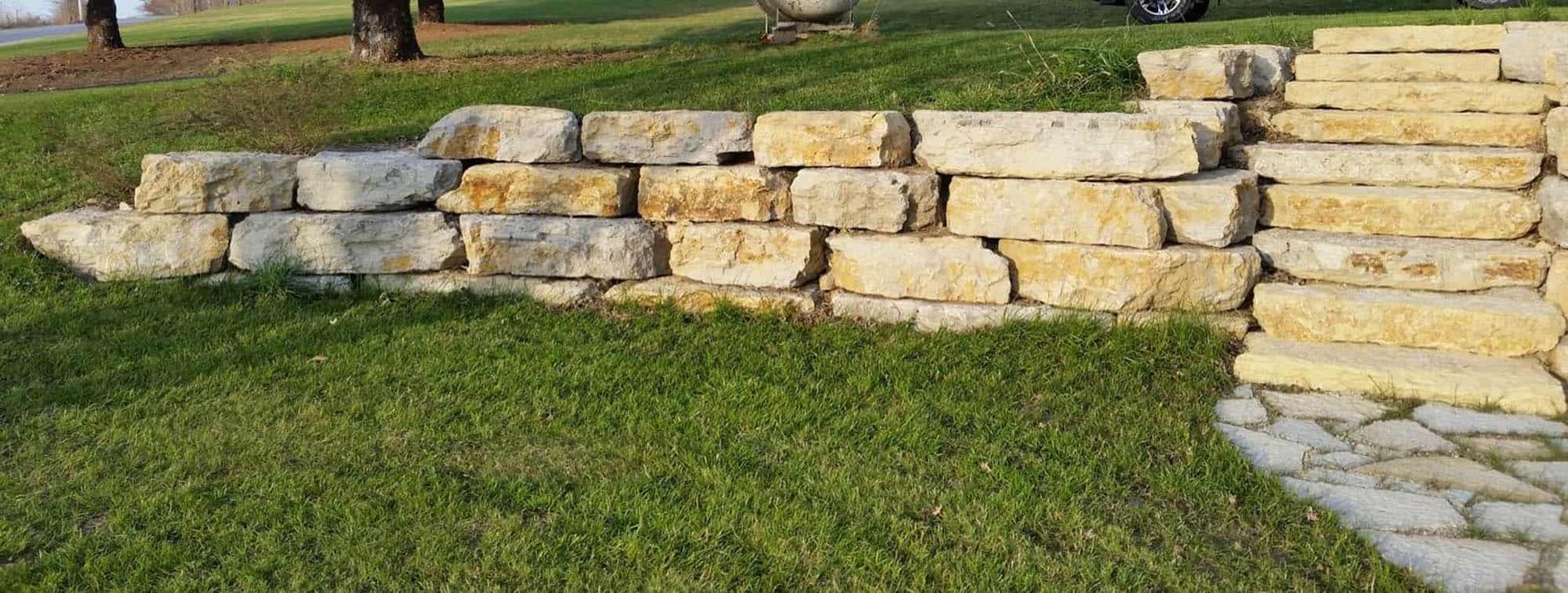A stone wall with stairs leading up to it is in the middle of a lush green field.