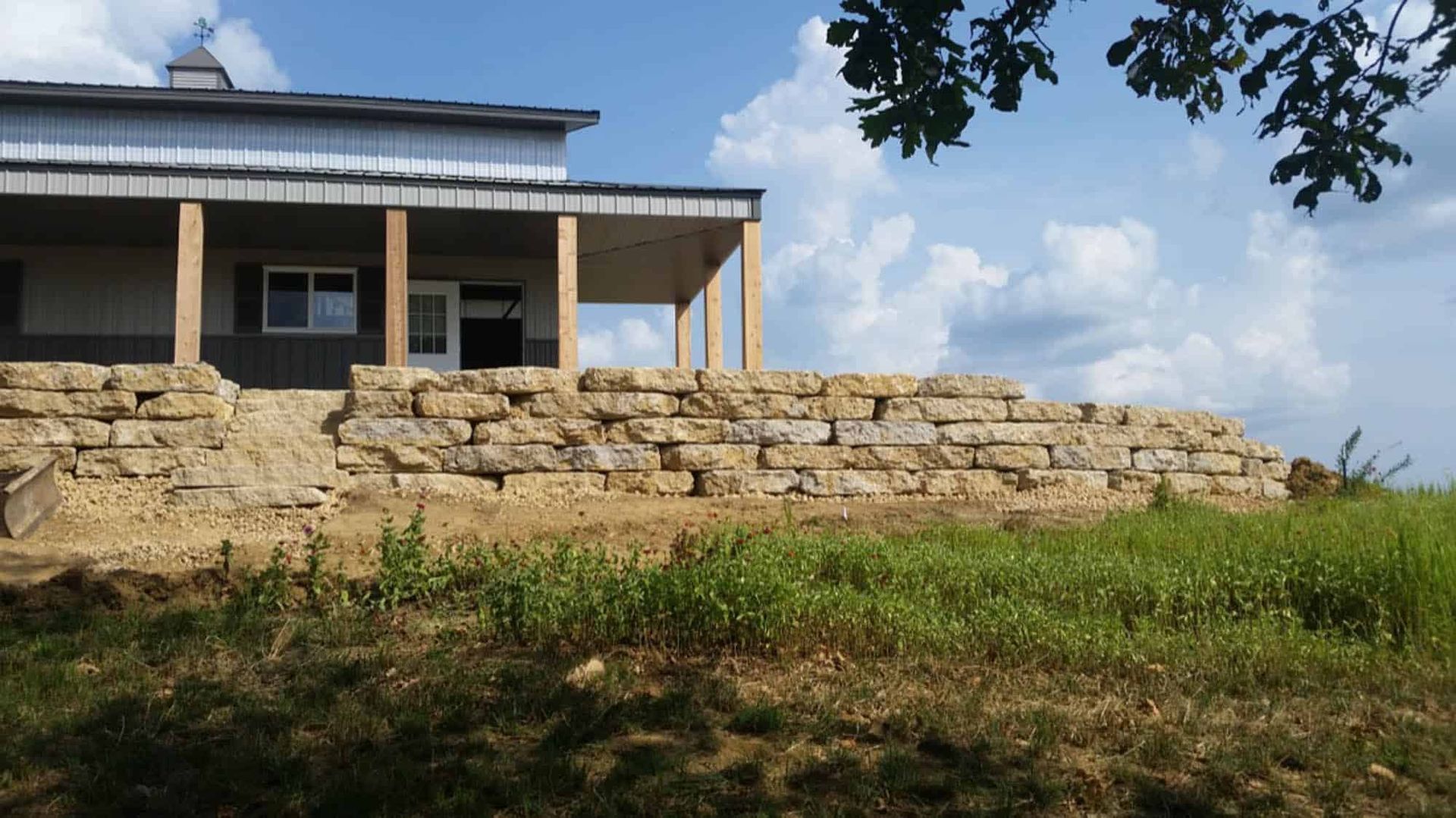 A house is sitting on top of a hill with a stone wall in front of it.