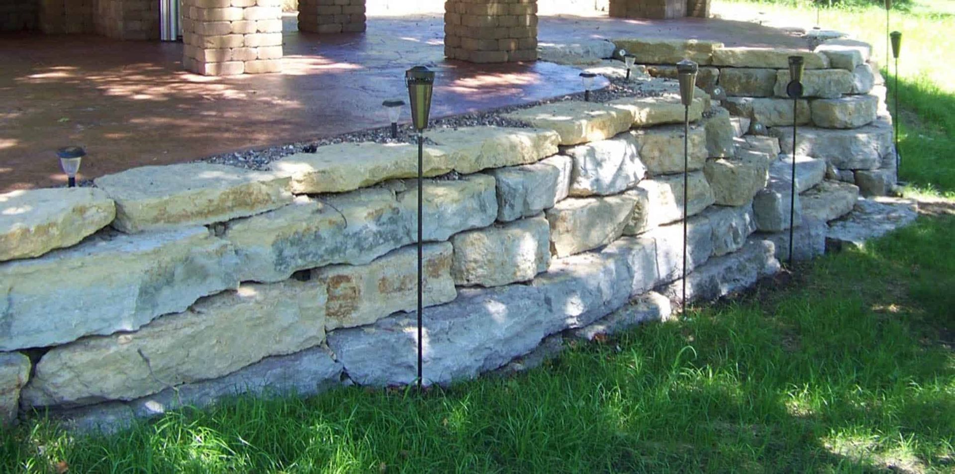 A stone wall with a patio in the background