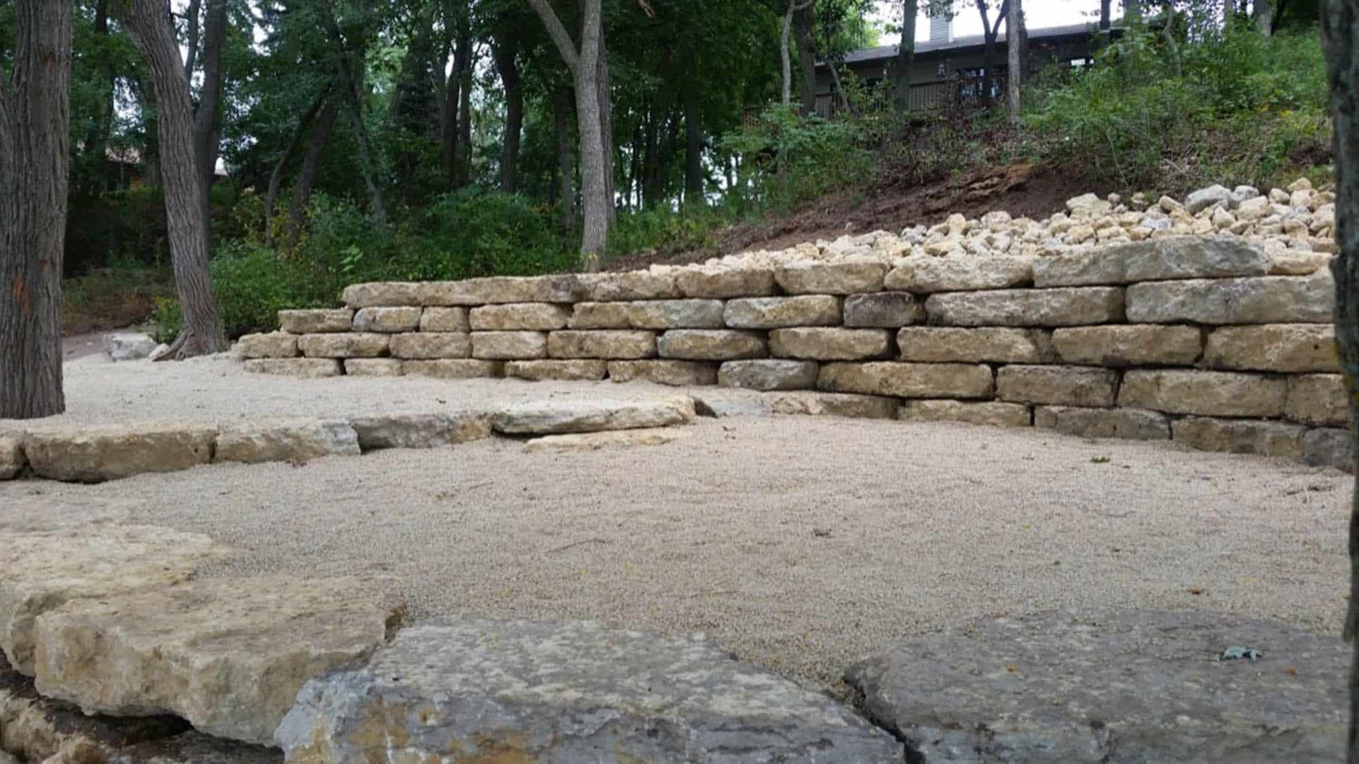 A stone wall is surrounded by trees and gravel in a park.