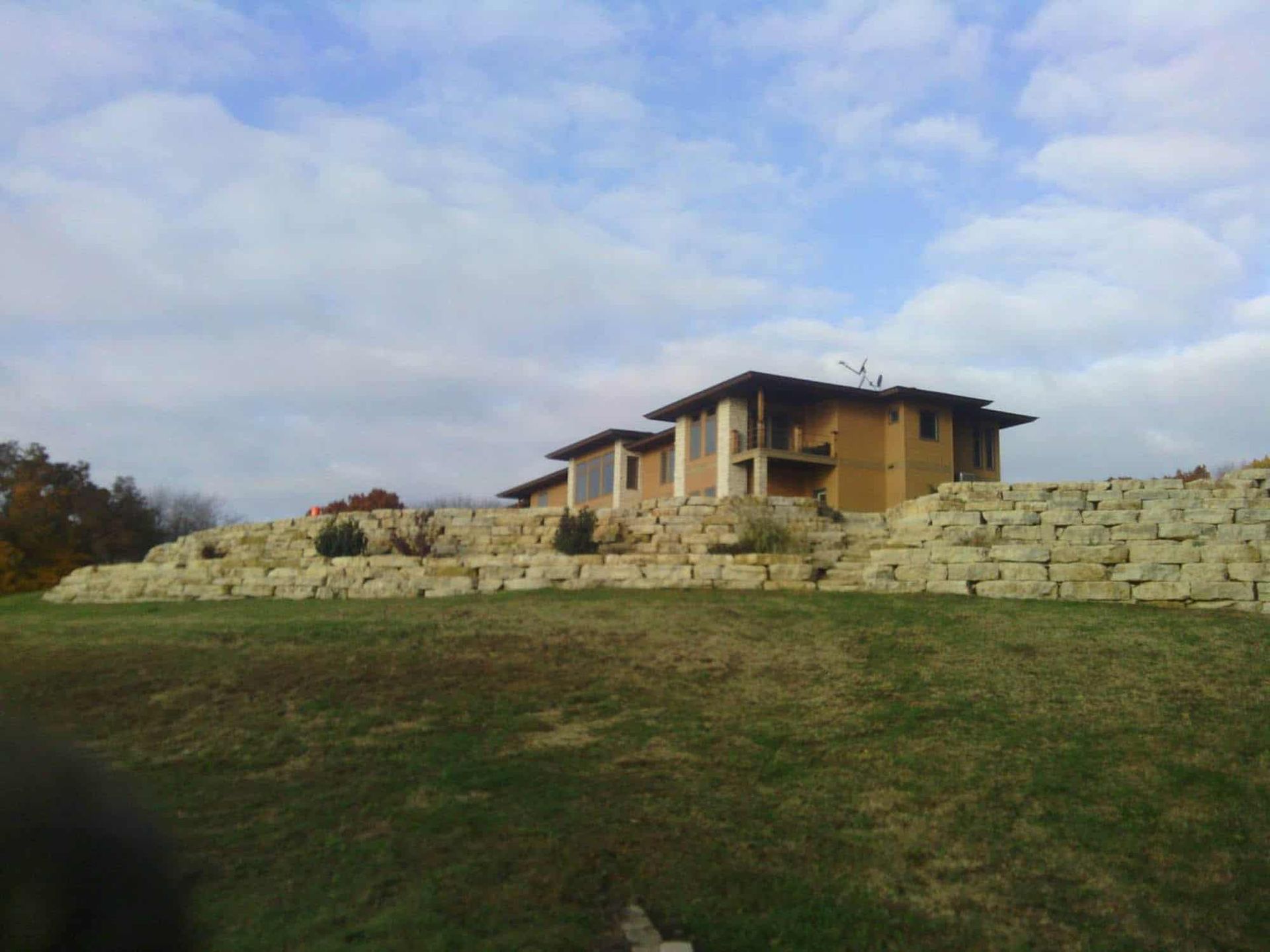 A house is sitting on top of a hill with a stone wall surrounding it.