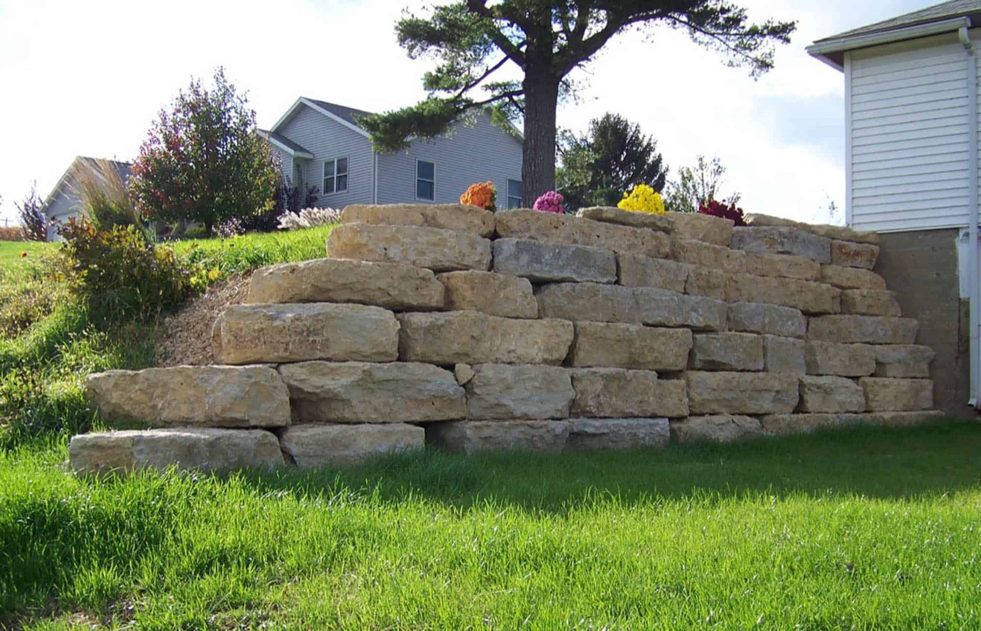 A large stone wall is sitting in the grass in front of a house
