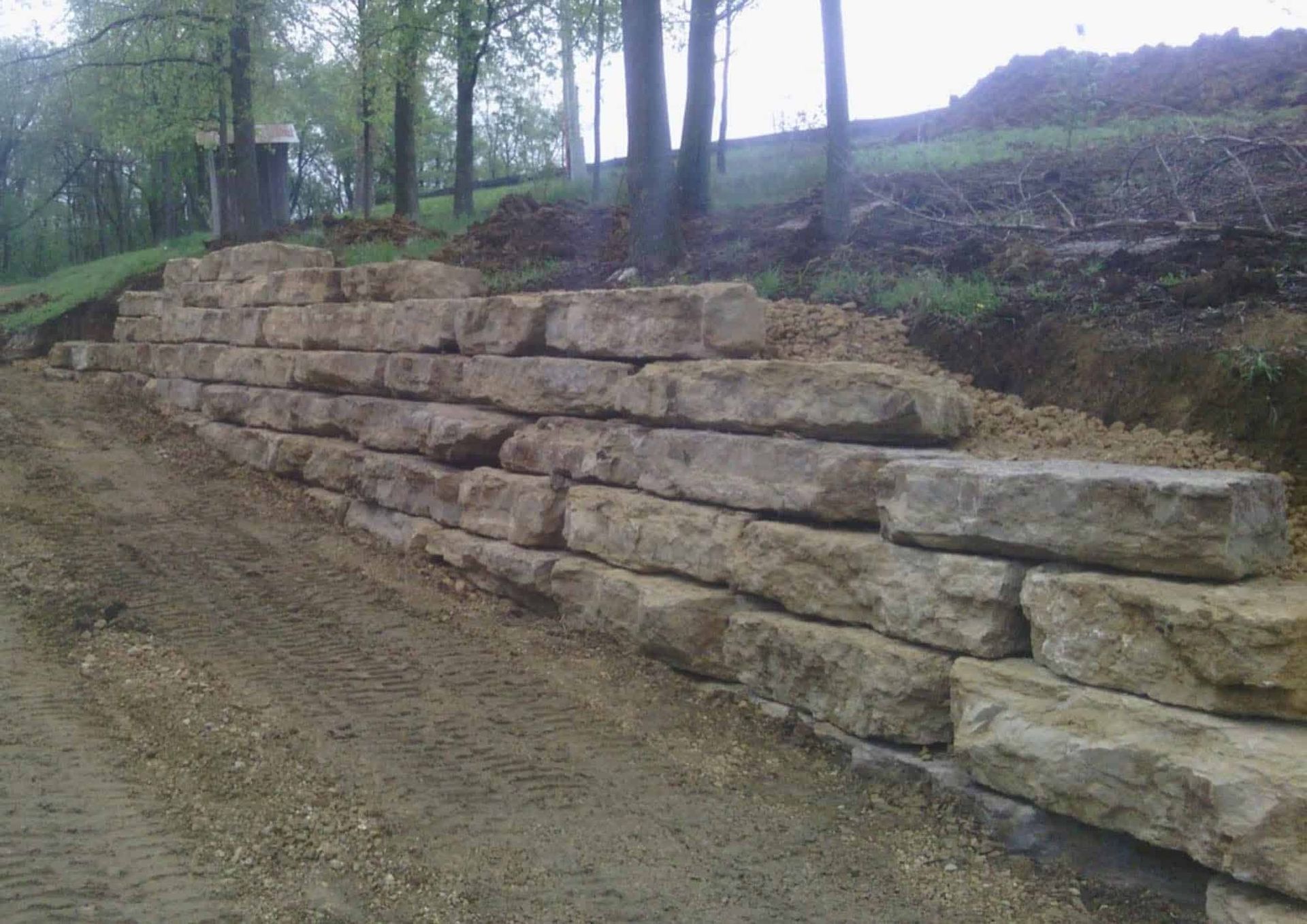 A large stone wall is sitting on the side of a dirt road.