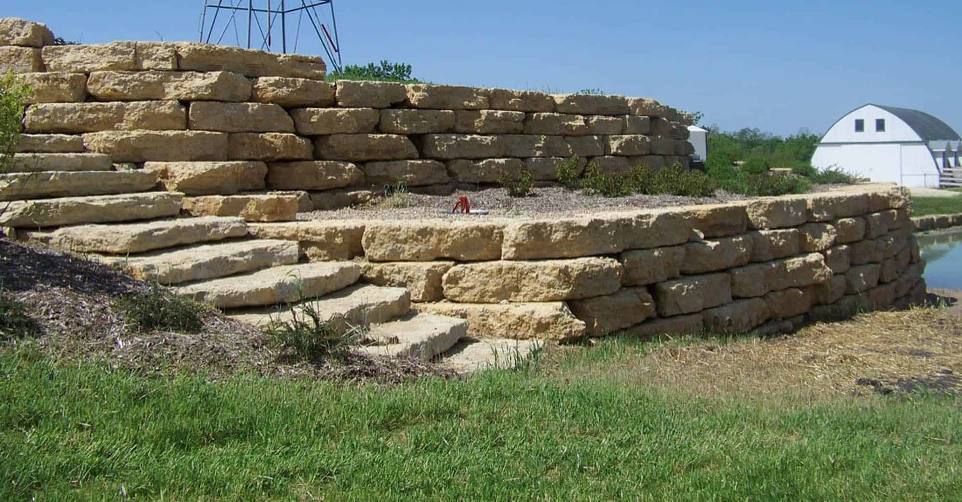 A large stone wall with a white barn in the background