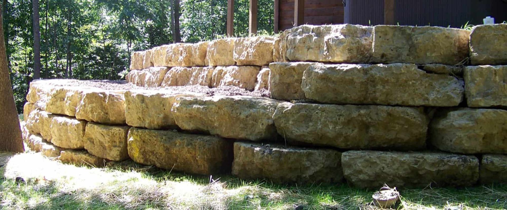 A large stone wall is sitting in the grass in front of a house.