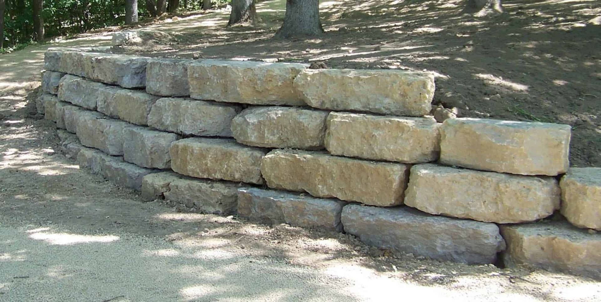 A stone wall is sitting on the side of a dirt road.