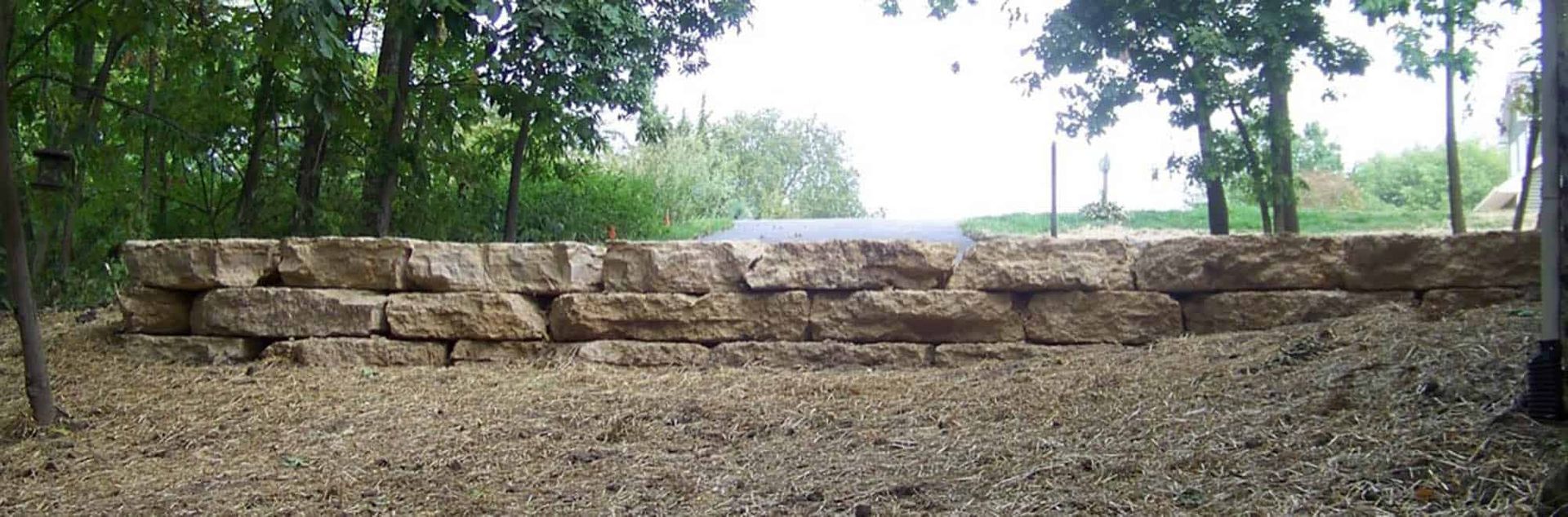 A stone wall in the middle of a forest with trees in the background.