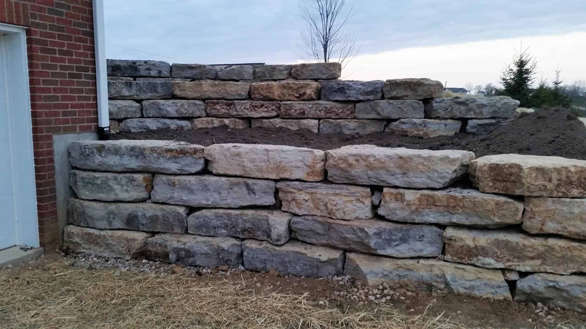 A large stone wall is being built in front of a brick building.