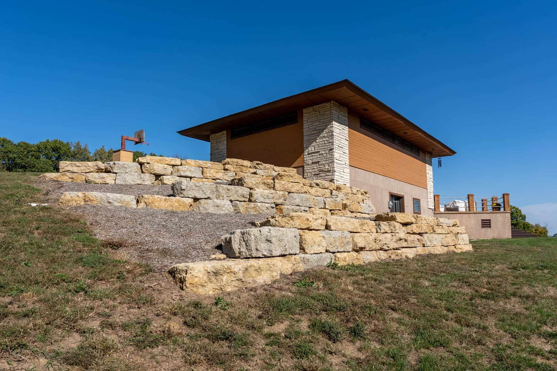 A house is sitting on top of a grassy hill next to a stone wall.
