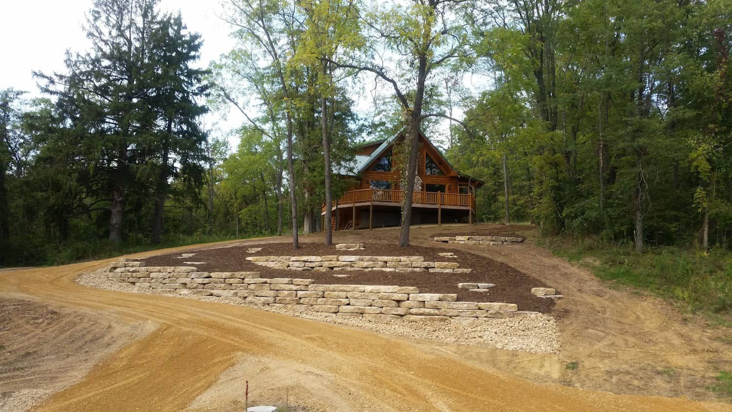 A log cabin is sitting on top of a dirt hill in the middle of a forest.
