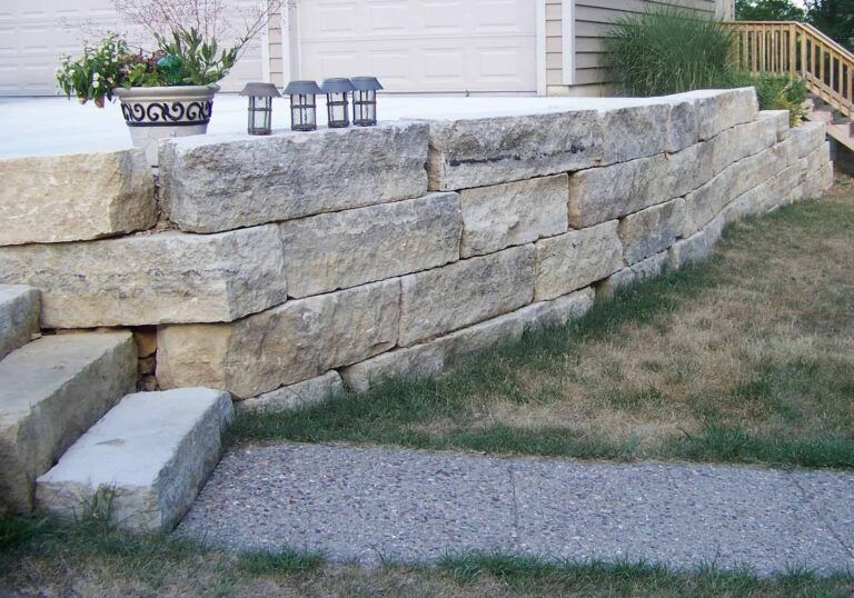 A stone wall with stairs leading up to it in front of a house