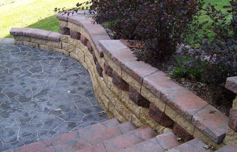 A stone wall surrounds a set of stairs in a backyard.