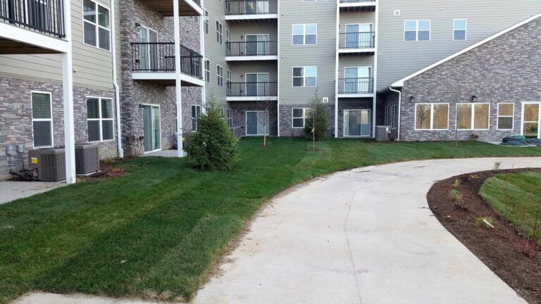 A concrete walkway leading to a large apartment building.