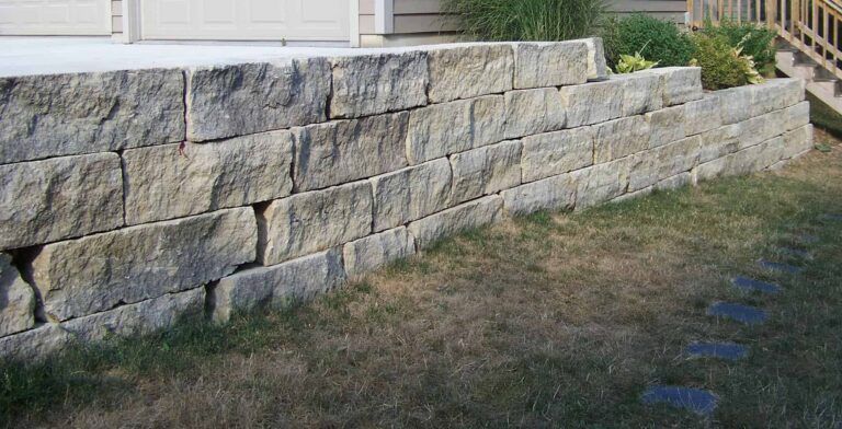 A large stone wall is sitting in the grass in front of a house.