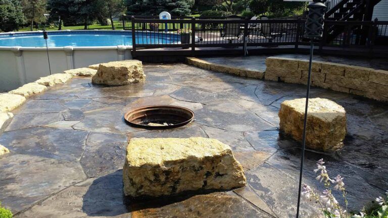 A fire pit on a patio next to a pool.