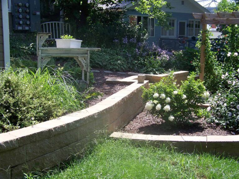 A garden with a brick wall and flowers in front of a house.