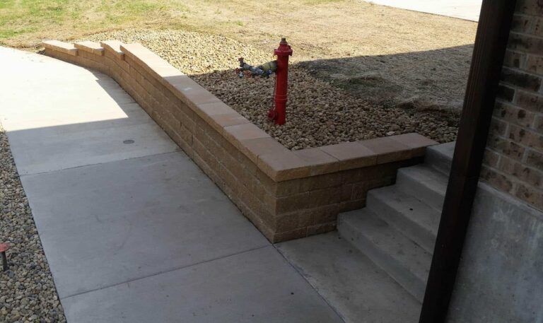 A red fire hydrant is next to a brick wall and stairs.