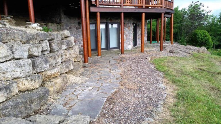A stone walkway leading to a large house with a wooden deck.