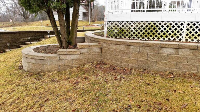 A brick wall with a tree in the middle of it in front of a house.