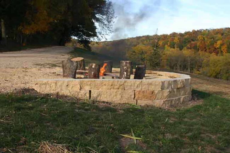 A fire pit in the middle of a field with trees in the background.