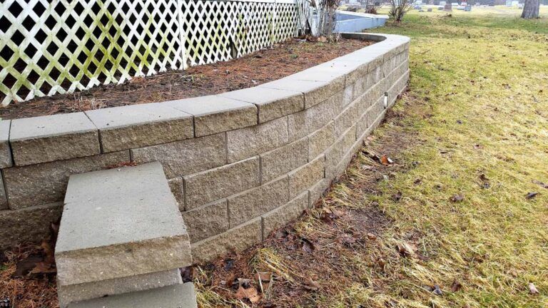 A brick wall in a yard with a fence in the background.