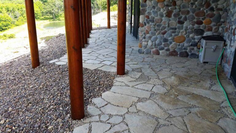 A stone walkway with wooden pillars and a green hose.