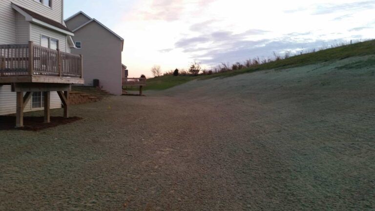 A driveway leading to a house with a deck and a house in the background.