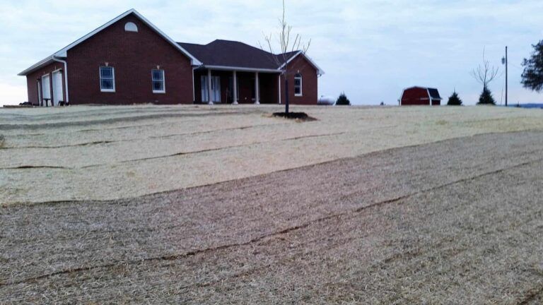 A brick house sits in the middle of a gravel field