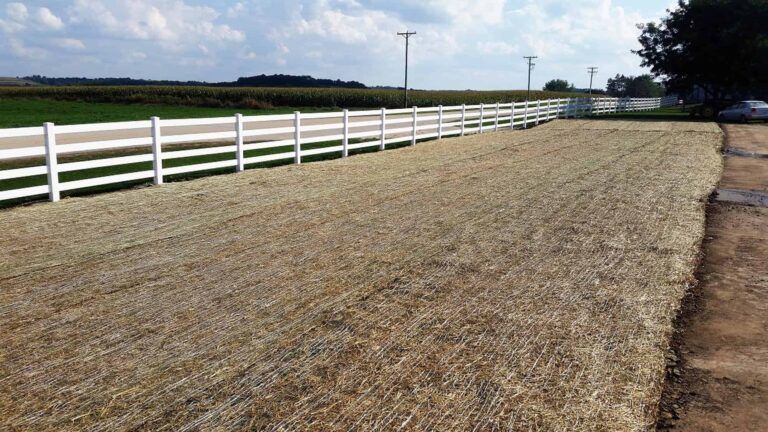 A white fence surrounds a field of hay