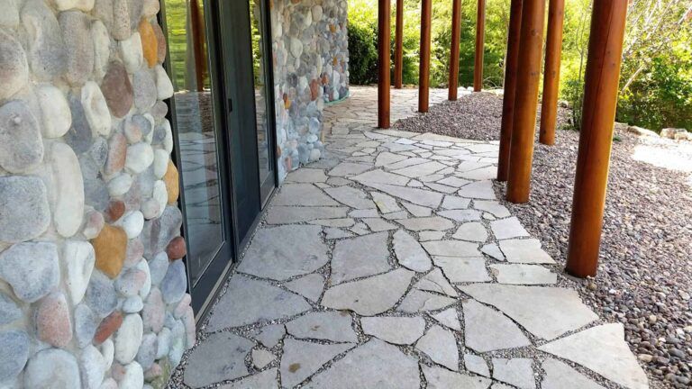 A stone walkway leading to a building with a stone wall and wooden pillars.