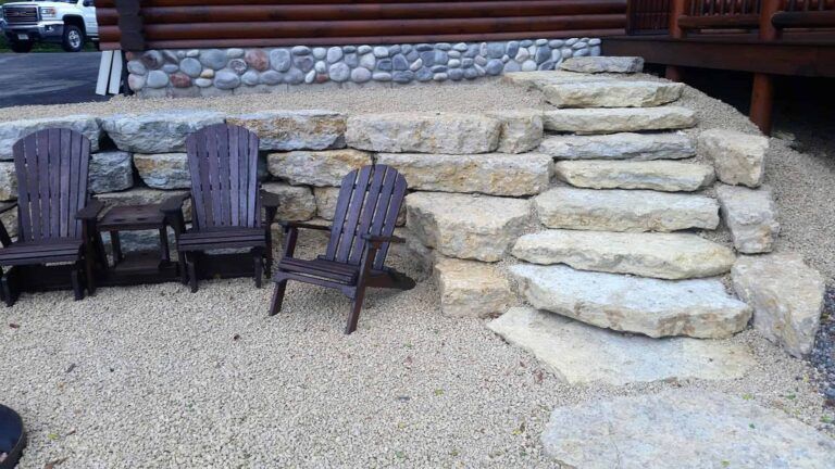 A stone wall with stairs and chairs in front of a log cabin.