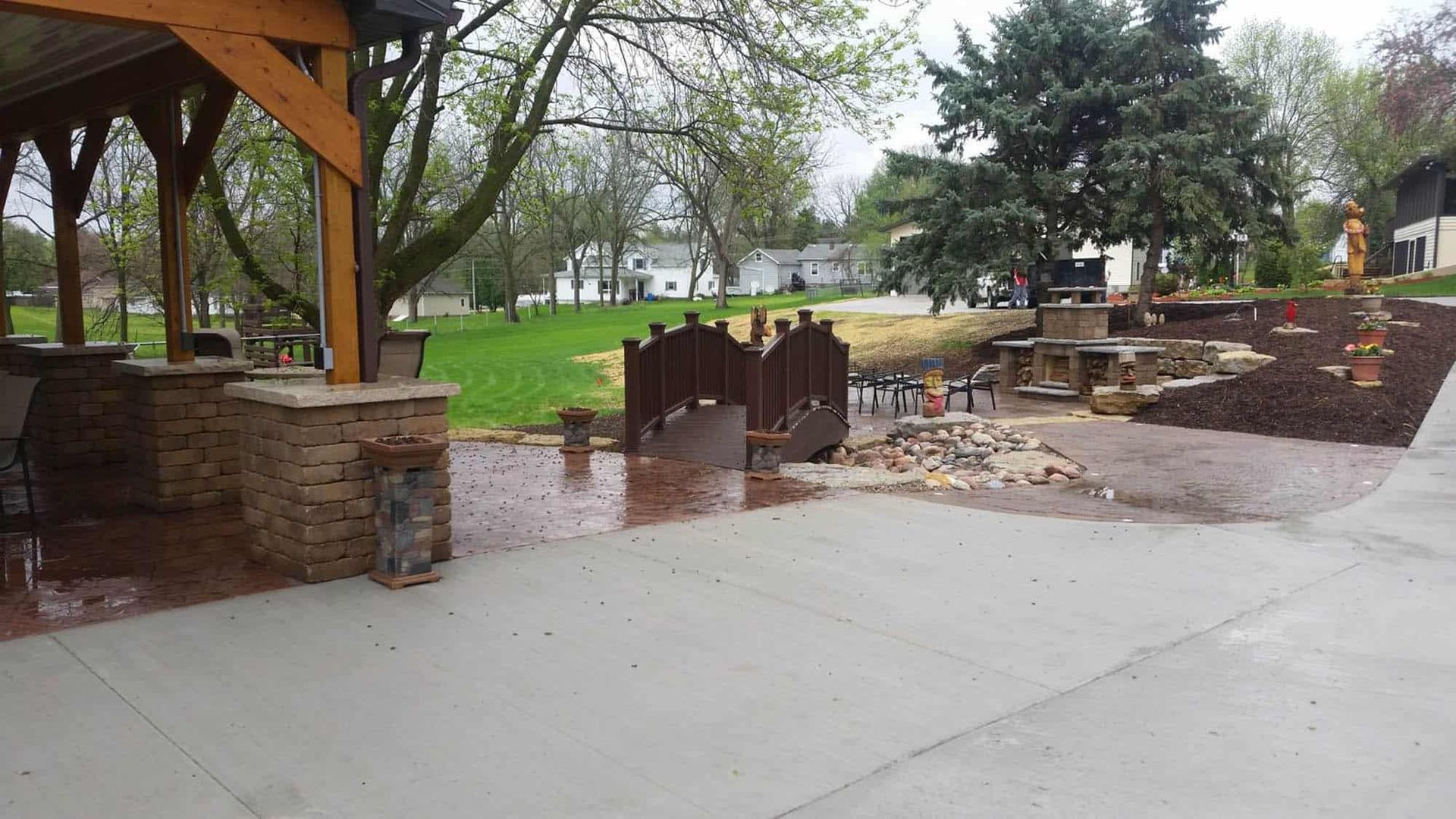 A concrete walkway leading to a park with a wooden bridge.